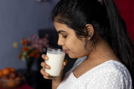 an Indian asian woman holding a glass of milk and drinking