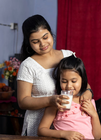 An Indian Asian mother giving glass of milk to her daughterの写真素材
