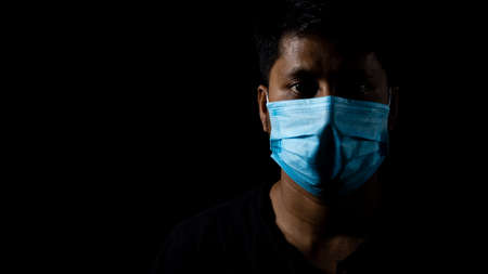 Low key face of an Indian asian male with surgical nose mask on black backgroundの写真素材