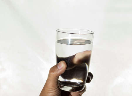 A glass of water held in human hand on white backgroundの写真素材