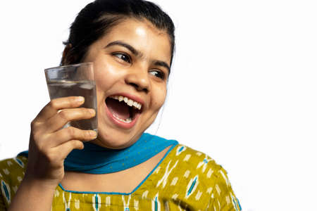 An Indian Asian woman with a glass of cold water touching on her cheek on white background
