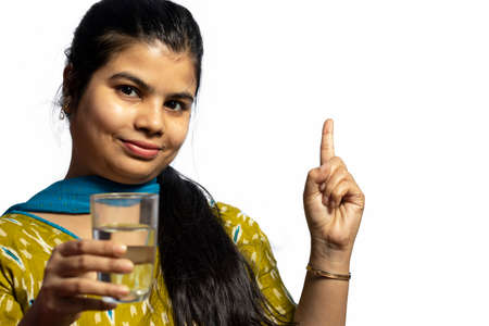 An Indian Asian woman with glass of water pointing on white background