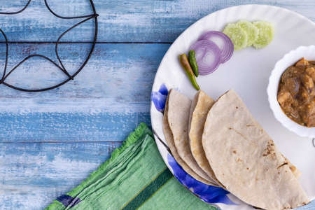 Top view of roti and curry with salad served in a plate on blue wooden table