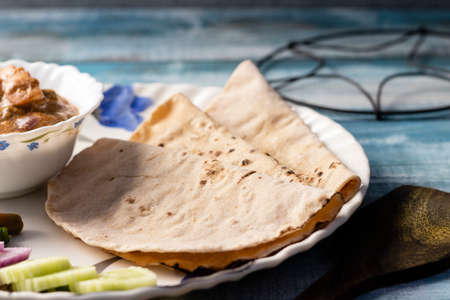 High angle view of roti and curry with salad served in a plate on blue wooden table