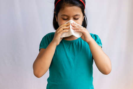 An Indian girl child sneezing with napkin or tissue paper on white background