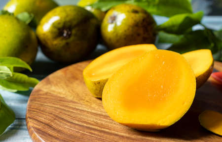 Selective focus on ripe mango slices on wooden chopping board along with mangoes and leaves on...