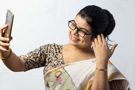 A beautiful indian woman in saree on white background taking selfie with smart phoneの写真素材