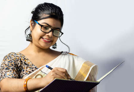 Isolated on white background an Indian office woman in saree writing on notebook with penの写真素材