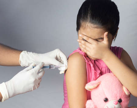 An Indian girl child with teddy bear in lap receiving vaccine dose on white background