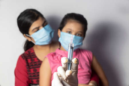 An Indian girl child in nose mask with mother waiting for vaccine doseの写真素材