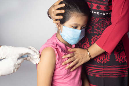 An Indian girl child in nose mask with mother receiving vaccine doseの写真素材