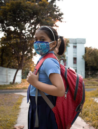 Portrait of a happy Indian girl child student in blue school uniform with red bag and nose mask protection going to schoolの写真素材