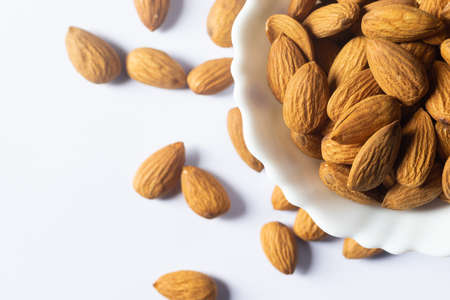 Close up top view of almond nuts in a white bowl on white backgroundの写真素材
