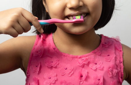 Close up view of an Indian girl child brushing teeth on white background