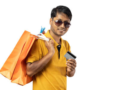 A middle aged Indian man in yellow dress with shopping bags and credit card smiling at the camera on...