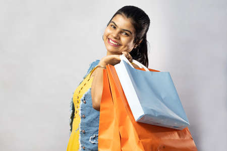 A beautiful Indian woman in yellow dress with shopping bags looking at the camera on white backgroundの写真素材