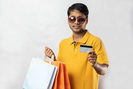 A middle aged Indian man in yellow dress with shopping bags and credit card smiling at the camera on...