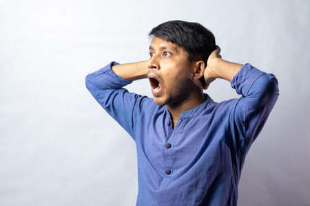 A young Indian male in blue dress with surprised look on white backgroundの写真素材