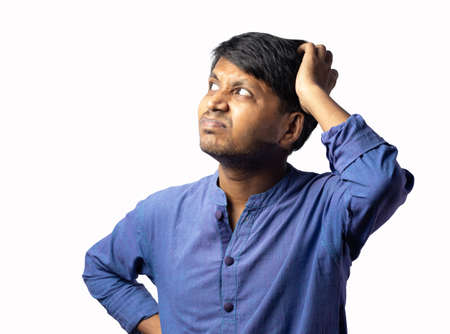 A young Indian male in blue dress scratching head and thinking on white background