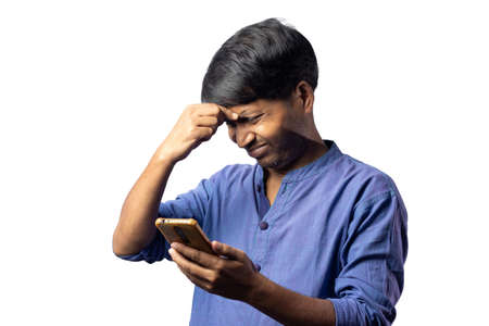 A young Indian male in blue dress facing headache with smart phone in hand on white backgroundの写真素材