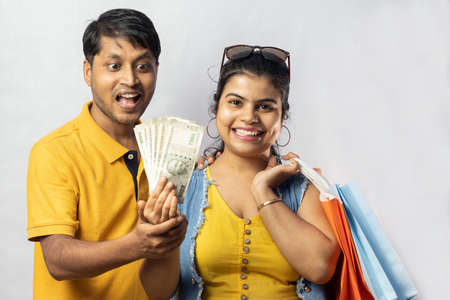 Indian couple in yellow dress with shopping bags and big savings smiling on white backgroundの写真素材