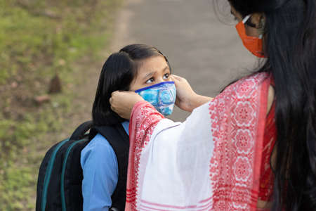 An Indian school girl child going to school again after pandemic with her mother wearing nose mask protectionの写真素材