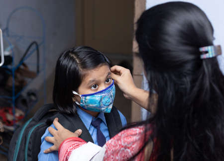 An Indian mother preparing her girl child with nose mask protection to send to school after pandemicの写真素材