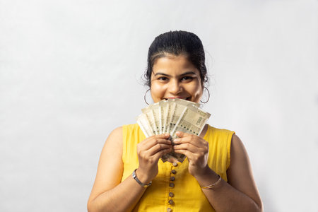 A beautiful Indian woman in yellow dress with cash smiling at the camera on white backgroundの写真素材