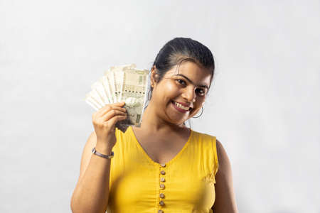 A beautiful Indian woman in yellow dress with cash smiling at the camera on white background