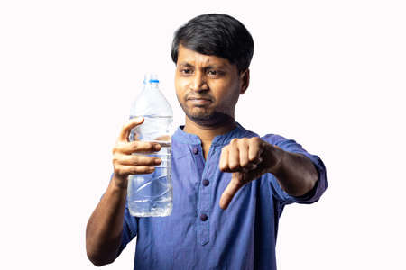 A young Indian male in ethnic dress shows thumb down to plastic bottles on white background