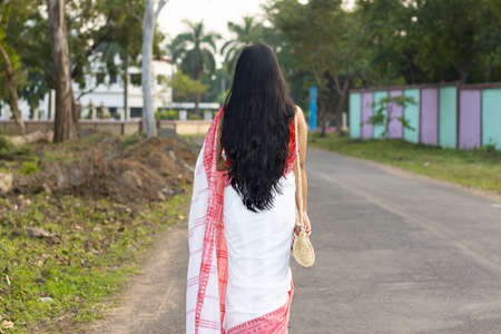 Back side of a pretty Indian woman in red saree and long hair walking on roadの写真素材