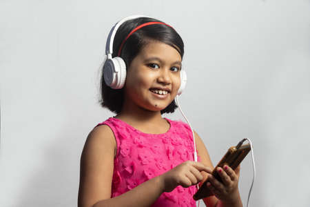 A cute Indian girl child listening to music from smart phone on white backgroundの写真素材