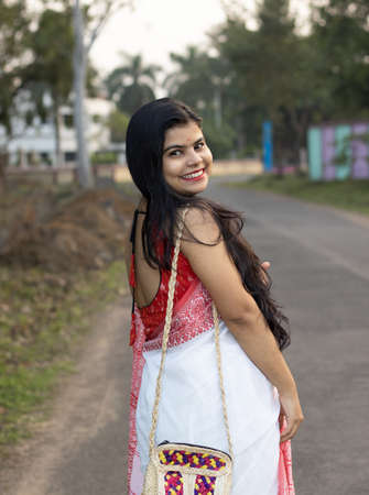 A pretty Indian woman in red saree and long hair posing for camera on roadの写真素材