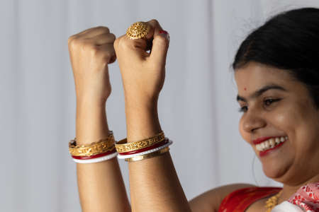 Selective focus on hands of an Indian woman in red saree wearing bangles with smiling face on white...
