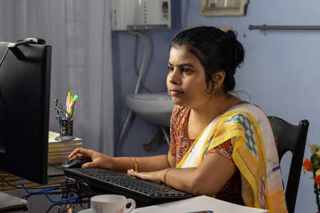 Indian woman in saree working on computer at home, work from home concept