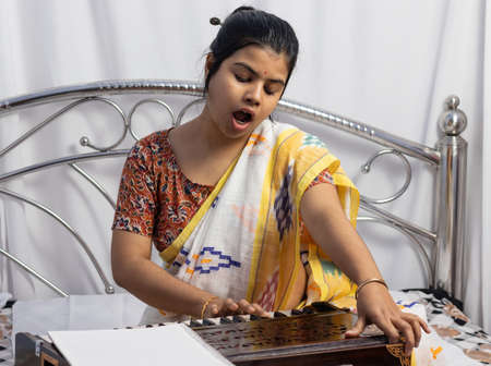 A beautiful Indian woman in saree singing and playing harmonium on white background