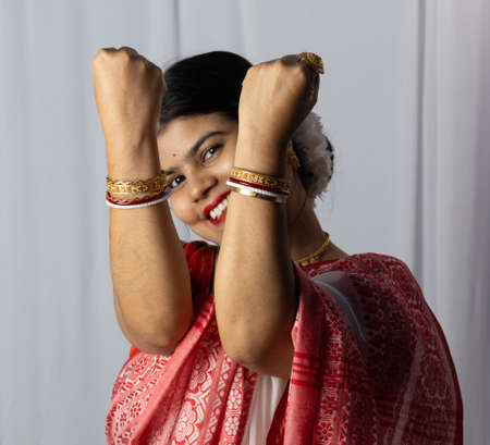 Selective focus on hands of an Indian woman in red saree wearing bangles with smiling face on white backgroundの写真素材