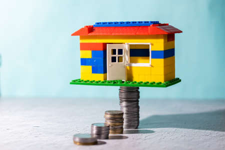 A toy house placed on stacks of coins on blue background: savings concept
