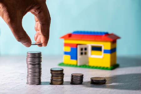 Selective focus on human hand building stacks of coins in front of a toy home: savings conceptの写真素材
