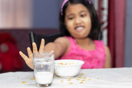 Selective focus on an Indian girl child with incomplete meal of cornflakes and milk showing dislikeの写真素材
