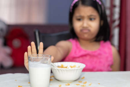 Selective focus on an Indian girl child with incomplete meal of cornflakes and milk showing dislikeの写真素材