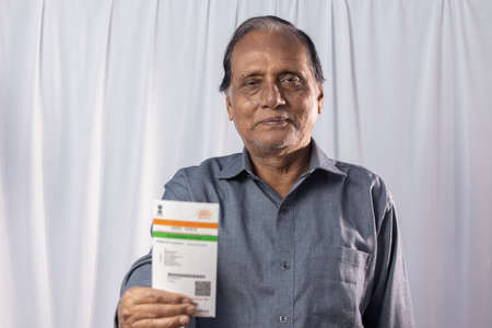 An Indian old man smiling with Aadhaar card in hands on white backgroundの写真素材