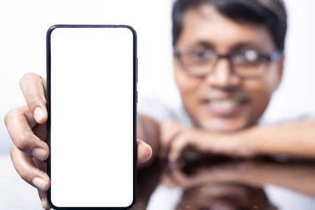 Close up of a white blank smart phone screen held in hand by an Indian smiling maleの写真素材