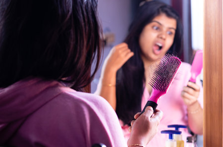 Selective focus on a pink hair brush full of fallen hair held in hand by a worried Indian woman in...