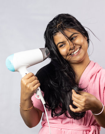 A pretty Indian woman drying black hair with hair dryer on white white backgroundの写真素材