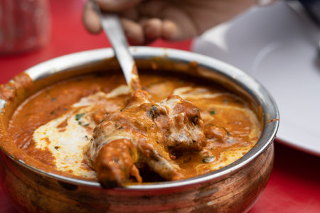Close up view of a bowl of chicken butter masala - an Indian food served on red table