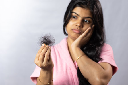 Selective focus on fallen hair held in hand by a worried Indian woman on white backgroundの写真素材