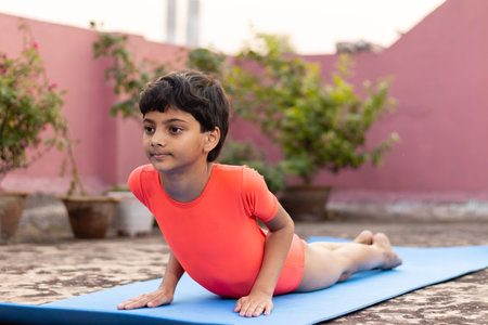 An Indian girl child practicing Bhujangasana or cobra pose yoga on yoga mat outdoors