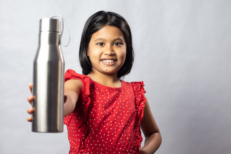 An Indian asian girl child in red dress with a stainless steel bottle of water on white backgroundの写真素材