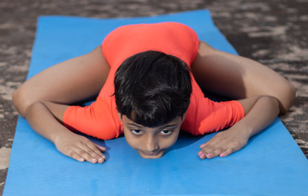 An Indian girl child practicing vekasana yoga on yoga mat outdoorsの写真素材